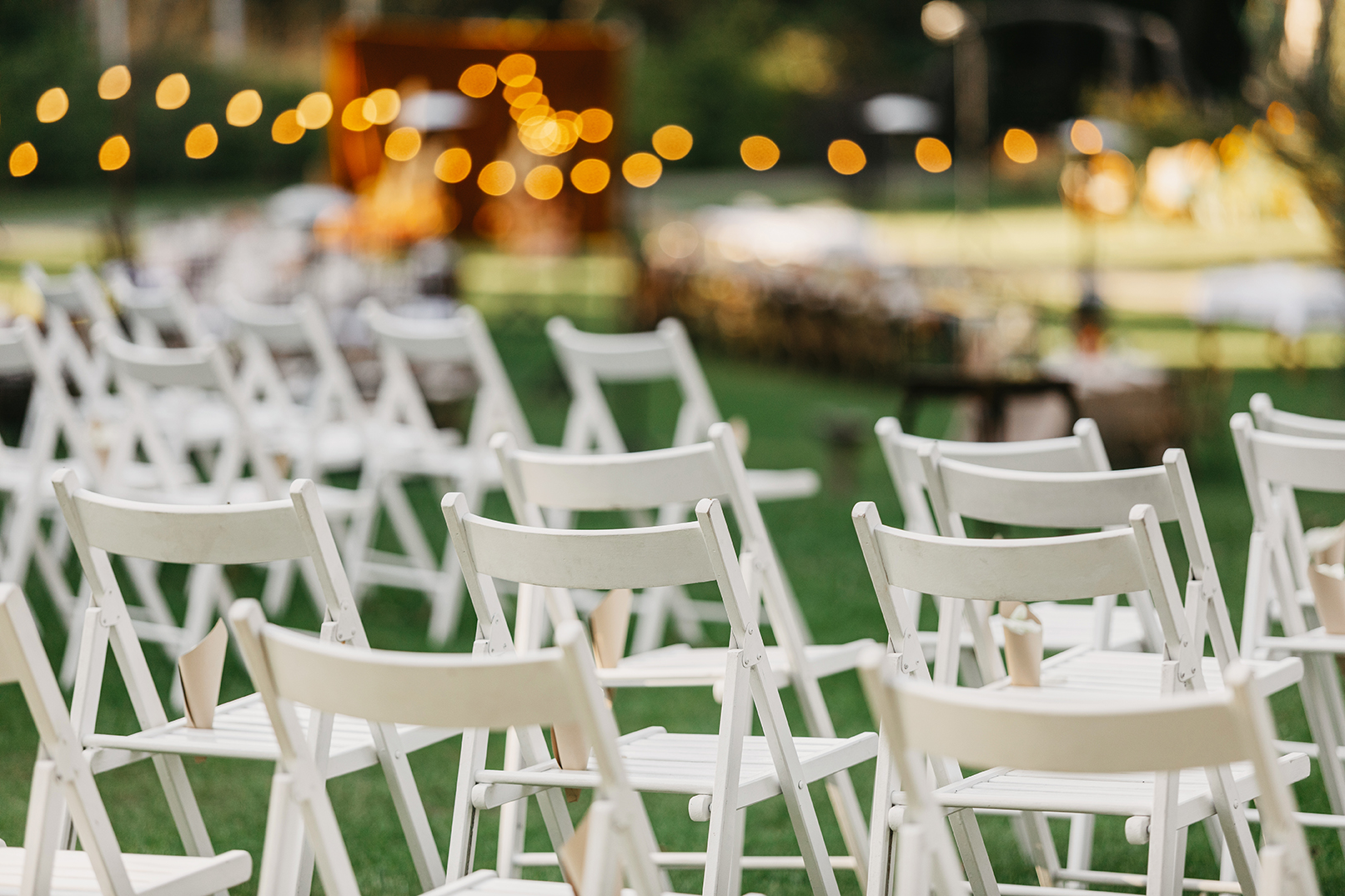 Modern stylish outdoor wedding, catering and design of rite. A lot of white folding chairs with paper packages with petals on green lawn for marriage ceremony in summer, flat lay, nobody, free space